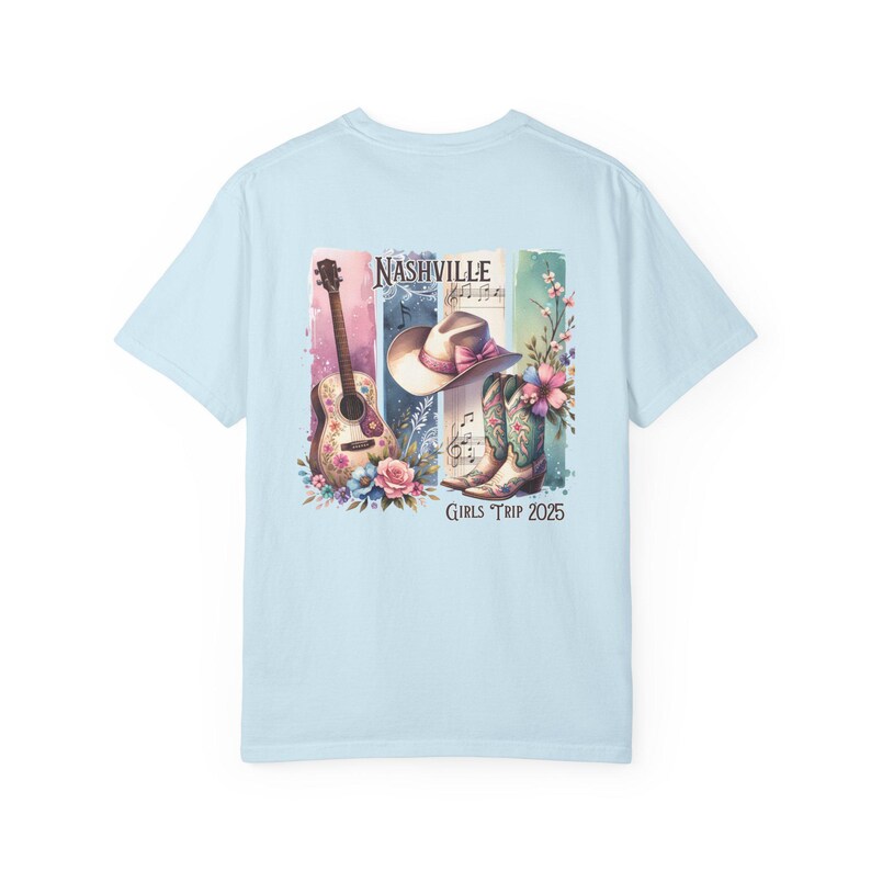 May include: Light blue t-shirt featuring a watercolor design with a guitar, cowboy hat, and boots. The word "Nashville" is above the illustrations, with the text "Girls Trip 2025" below. Floral accents are included.