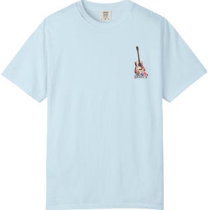 May include: Light blue t-shirt with a small graphic of a guitar and flowers, with the word "Nashville" printed below. The shirt is made of a soft material and has a classic crew neck.