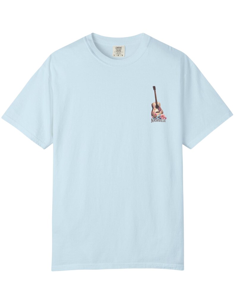 May include: Light blue t-shirt with a small graphic of a guitar and flowers, with the word "Nashville" printed below. The shirt is made of a soft material and has a classic crew neck.
