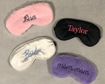 May include: Four sleep masks in the image. A pink, fluffy sleep mask with "Lisa" embroidered in black. A black satin sleep mask with "Taylor" in pink. A white satin sleep mask with "Bride" in blue. A purple, fluffy sleep mask with "mom mom" in black.
