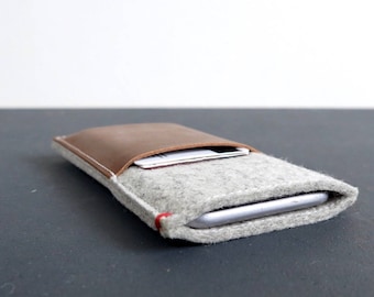 May include: A gray felt phone case with a brown leather flap and red stitching. The case is lying on a gray surface.