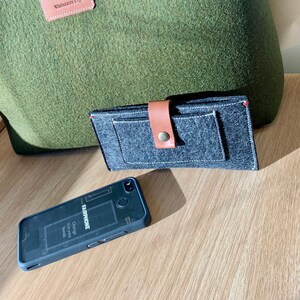 May include: A green felt tote bag with a brown leather handle and a label that says "Wanderlust Co.". A gray felt wallet with a brown leather strap and a black felt phone case are also pictured.