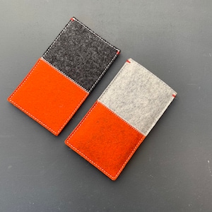 May include: Two felt phone cases, one with a black and orange color scheme and the other with a gray and orange color scheme.