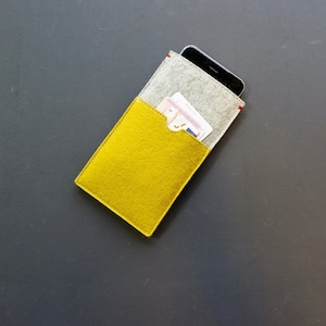 May include: A yellow felt phone case with a grey felt pocket for cards. The case is closed and has a red stitch detail.