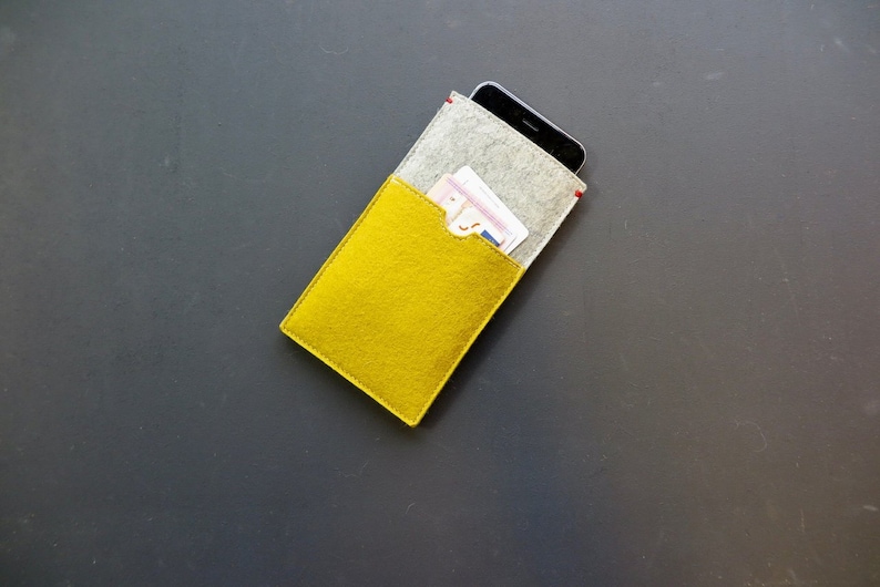 May include: A yellow felt phone case with a grey felt pocket for cards. The case is closed and has a red stitch detail.