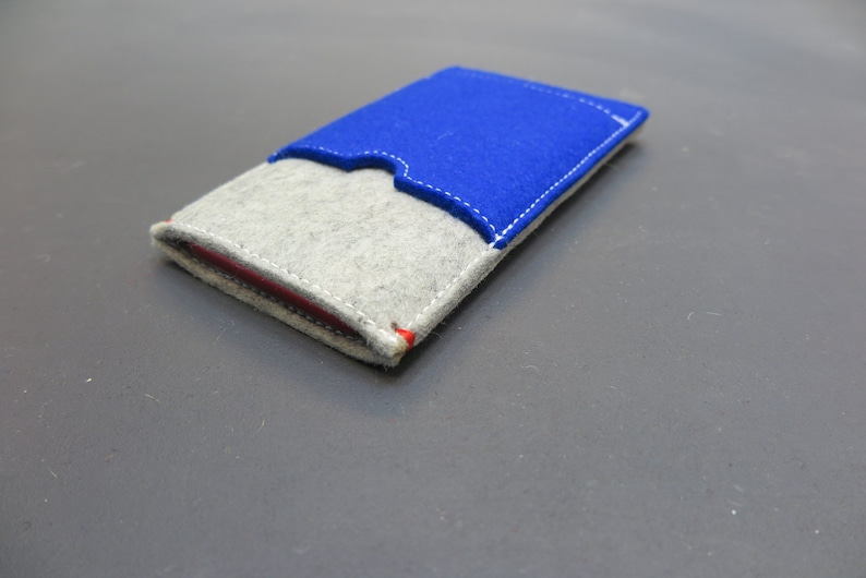 May include: A small grey felt wallet with a blue felt flap. The wallet has white stitching around the edges and a red accent on the flap.