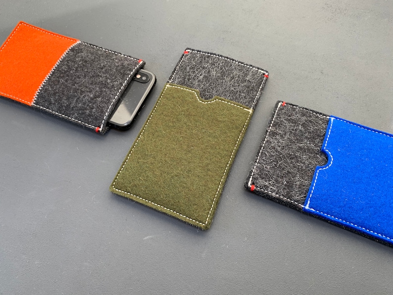 May include: Three felt phone cases in different colours. The first case is orange and grey, the second is green, and the third is grey and blue.
