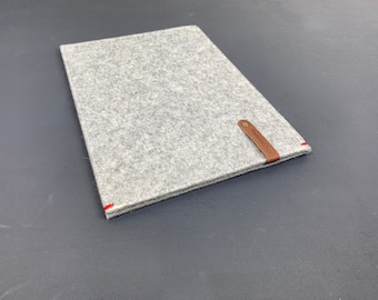 Puede incluir: Una funda para portátil de fieltro gris con una correa de cuero marrón y el texto "Remarkable" en la correa. La funda tiene costuras rojas alrededor de los bordes.