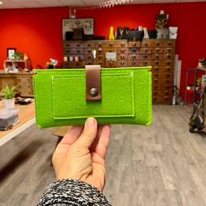 May include: A bright green felt phone case with a brown leather strap and a metal button. The case has a small pocket on the front.