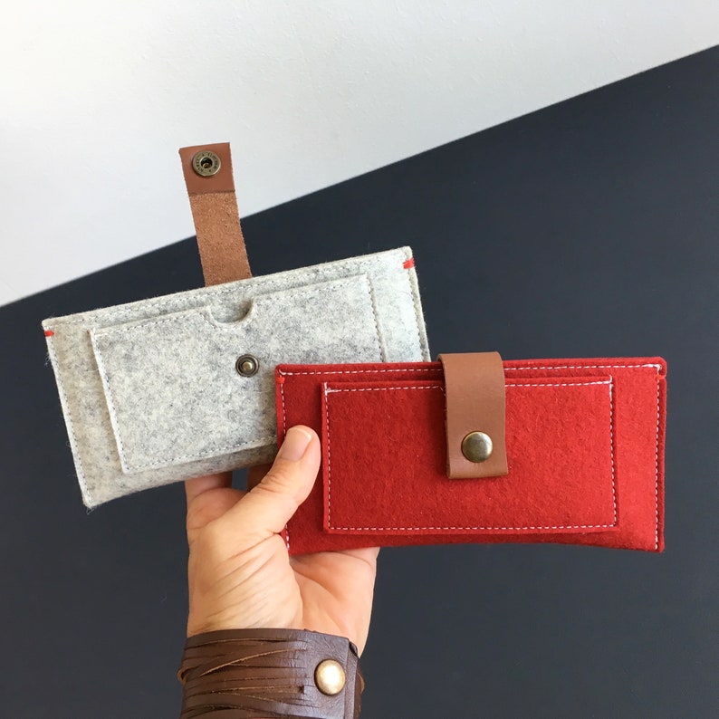 May include: Two felt phone cases, one gray and one red. The gray case has a flap and a brown leather strap. The red case has a brown leather strap and a white stitch detail.