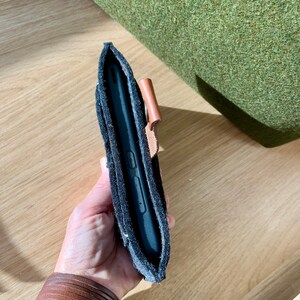 May include: A black phone case with a brown leather strap. The case is made of a soft, textured material and has a flap that covers the phone screen.