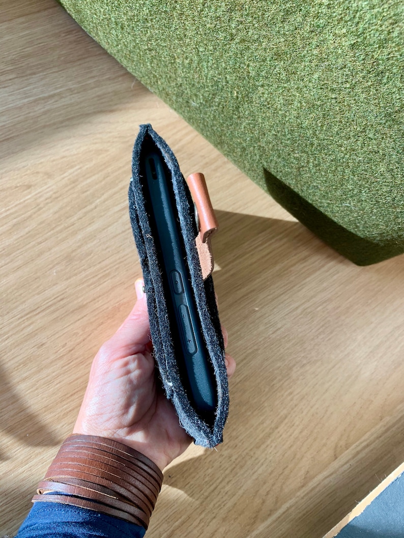 May include: A black phone case with a brown leather strap. The case is made of a soft, textured material and has a flap that covers the phone screen.