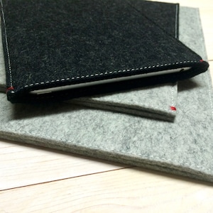 Peut inclure: Un ensemble de trois pochettes pour tablette en feutre gris et noir. Les pochettes sont faites d'un matériau en feutre doux et durable et ont un design simple et minimaliste.