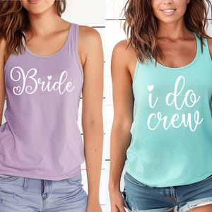 May include: Two sleeveless tank tops, one lilac and one turquoise, with white script. The lilac tank top says "Bride" with a heart, and the turquoise tank top says "i do crew" with a heart.