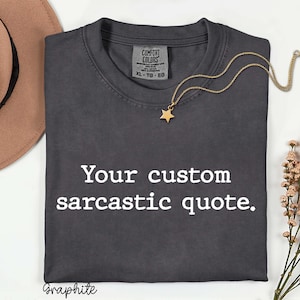 May include: A graphite grey short-sleeve t-shirt with a crew neckline and the white text "Your custom sarcastic quote." printed on the front. The shirt features a Comfort Colors brand label at the inner neck, indicating a size XL.