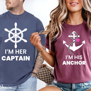 May include: A denim blue t-shirt with a white ship wheel graphic and the text I'M HER CAPTAIN, and a berry-colored t-shirt with a white anchor graphic, a black rope detail, a small pink heart, and the text I'M HIS ANCHOR.