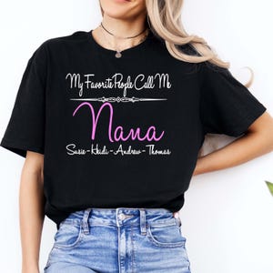 May include: Black t-shirt with the text "My Favorite People Call Me Nana" in white script above the pink word "Nana". Below the word "Nana" are the names Susie, Heidi, Andrew, and Thomas.