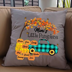 May include: Gray throw pillow with a fall-themed design. A teal truck with a black and white plaid design is carrying pumpkins with names on them. The truck is under a tree with orange leaves and butterflies. The text "Mimi's Little Pumpkins" is above the truck.
