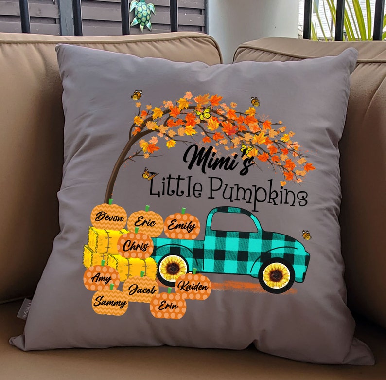 May include: Gray throw pillow with a fall-themed design. A teal truck with a black and white plaid design is carrying pumpkins with names on them. The truck is under a tree with orange leaves and butterflies. The text "Mimi's Little Pumpkins" is above the truck.