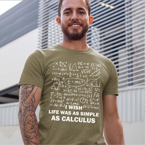 May include: An olive green short-sleeve t-shirt featuring a white graphic print of various mathematical equations and formulas. The text "I WISH LIFE WAS AS SIMPLE AS CALCULUS" is printed in white capital letters at the bottom of the design.