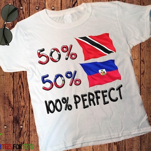 Puede incluir: Una camiseta blanca de manga corta con el texto 50% 50% 100% PERFECT. Los números están rellenos con las banderas de Trinidad y Tobago y Haití. Las banderas también aparecen por separado a la derecha de los porcentajes en un estampado.