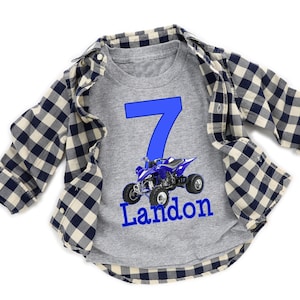 May include: A gray t-shirt with a blue number 7 and a blue and black ATV. The name Landon is written below the ATV.