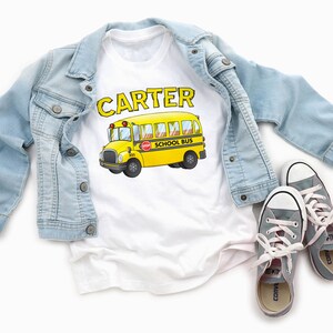 May include: White t-shirt with the name "CARTER" printed in black above a yellow school bus with the words "SCHOOL BUS" printed on the side.