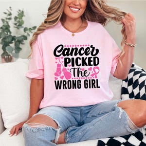 May include: Pink t-shirt with a black graphic that says "Cancer Picked The Wrong Girl" with pink boxing gloves and a pink ribbon.