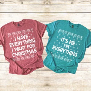 May include: Two short-sleeved t-shirts with Christmas-themed text. One is red with the text "I HAVE EVERYTHING I WANT FOR CHRISTMAS." The other is teal with the text "IT'S ME I'M EVERYTHING."