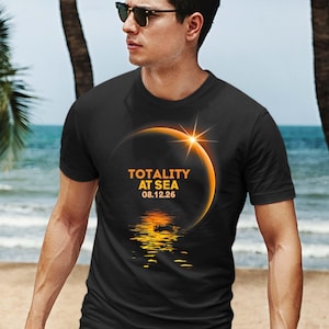 May include: A black t-shirt with a graphic of a solar eclipse over a body of water. The text "Totality at Sea 08.12.26" is printed on the shirt.