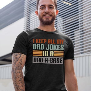 May include: A dark grey t-shirt with a vintage-style graphic that reads "I keep all my dad jokes in a dad-a-base".
