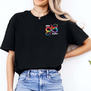 May include: A black short-sleeve t-shirt featuring a small graphic on the left chest. The design includes a colorful infinity symbol, a monarch butterfly, and the text "Autism Acceptance" written in a white script font.