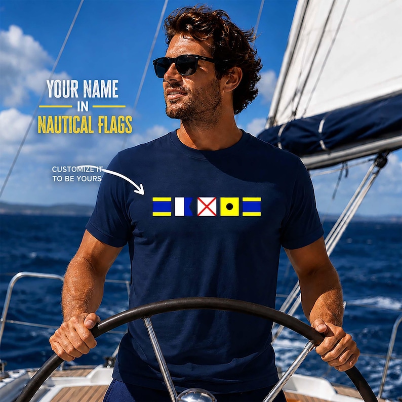 Custom Nautical Flag Shirt in navy blue featuring colorful maritime signal flags across the chest. A man in sunglasses steers a sailboat under a bright blue sky.