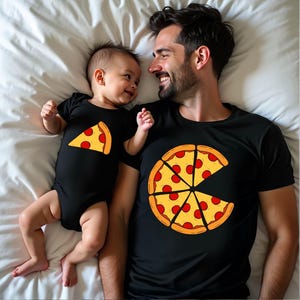 May include: A black baby bodysuit featuring a single yellow pizza slice graphic and a black t-shirt featuring a large yellow pizza graphic with one slice missing. Both garments are made of black fabric and display matching pepperoni pizza designs.