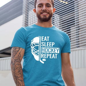 May include: A turquoise blue t-shirt with a white graphic of a hockey mask and the text "Eat Sleep Hockey Repeat".