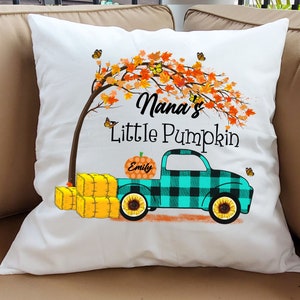 May include: White pillow with a fall-themed design featuring a truck with a pumpkin that says "Emily" on it. The truck is driving under a tree with orange and yellow leaves. The text "Nana's Little Pumpkin" is printed on the pillow.