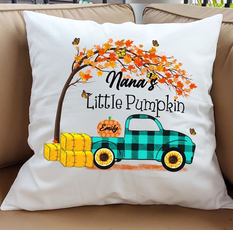 May include: White pillow with a fall-themed design featuring a truck with a pumpkin that says "Emily" on it. The truck is driving under a tree with orange and yellow leaves. The text "Nana's Little Pumpkin" is printed on the pillow.