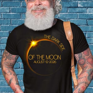 Peut inclure: Un t-shirt noir avec un graphique d'une éclipse solaire avec le texte "The Dark Side of the Moon August 12-2026".