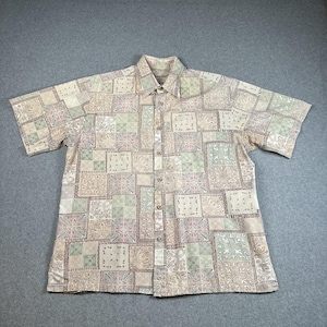 Puede incluir: Camisa de manga corta con botones y un patrón cuadrado repetitivo en beige, verde y rosa. La camisa tiene cuello y cierre de botones en la parte delantera. La tela parece ligera y adecuada para climas cálidos.