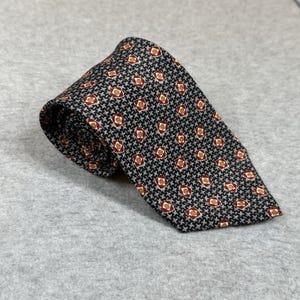 May include: A rolled-up necktie with a black and gray houndstooth pattern, accented with small red and gold geometric shapes. The tie is made of a smooth fabric and is suitable for formal or business attire.
