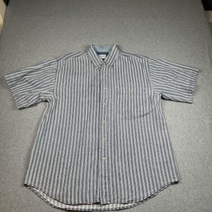 Pode incluir: Uma camisa abotoada de manga curta com listras verticais em tons de cinza e branco. A camisa tem um bolso no peito e uma gola abotoada. A camisa é feita de um tecido leve.