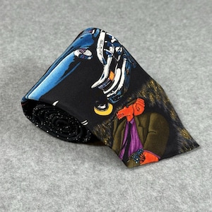May include: A rolled-up black necktie with a colorful graphic design. The design features a blue car, a red figure in a suit, and abstract white and yellow shapes. The tie is made of a smooth fabric and has a dotted pattern on the rolled edge.