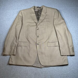 Peut inclure: Un blazer beige avec un motif à carreaux subtil. La veste a un revers cranté, une fermeture à trois boutons et deux poches avant. Les manches ont des poignets boutonnés. Le blazer est en tissu tissé.