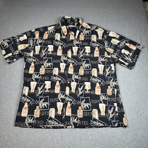 Peut inclure: Chemise noire à manches courtes avec un motif répété de bouteilles de bière, de verres et de feuilles tropicales en beige et blanc. La chemise a un col et est faite d'un tissu léger.