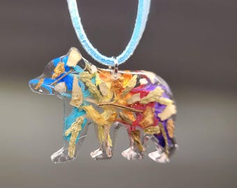 Puede incluir: Colgante de oso de resina transparente relleno de flores secas coloridas y detalles azules. El colgante cuelga de un cordón azul claro. Una joya única y artesanal.