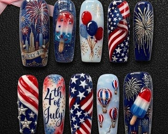 Pode incluir: Um conjunto de dez unhas artificiais com designs patrióticos. Cada unha apresenta um design diferente, incluindo fogos de artifício, a bandeira americana e picolés. A paleta de cores inclui vermelho, branco e azul, com detalhes em ouro e prata.