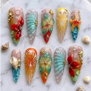 May include: A collection of ten long, almond-shaped acrylic nails with intricate designs. The nails feature a variety of colors, including red, orange, yellow, and blue, and are adorned with seashells, flowers, and other decorative elements. Some nails have gold accents.