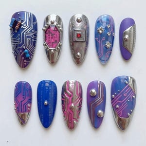 May include: A set of ten press-on nails featuring a cybernetic theme with metallic silver, blue, and purple gradients. Designs include printed circuit board patterns, binary code, small electronic components, embedded rhinestones, and studs.
