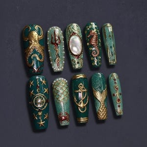 May include: A collection of ten long, coffin-shaped false nails in teal and gold. Each nail showcases detailed designs, such as an octopus, seahorse, mermaid tail, and nautical themes. Embellishments include pearls, glitter, and metallic accents.