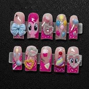 May include: A set of ten artificial nails with various designs. The nails have a light pink base with bright pink accents and decorations, including a blue bow, a cartoon character, lollipops, balloons, and heart-shaped embellishments.